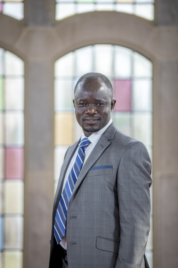 A well dressed professor stands in front of a window