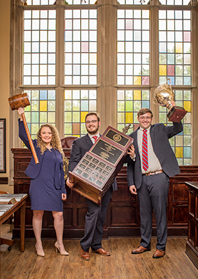 three students hold up trophies