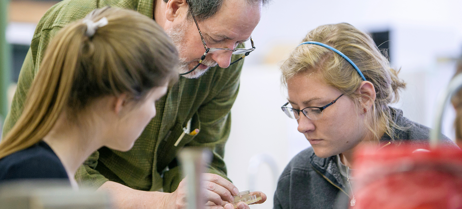 a male professor and two students look at a specimen