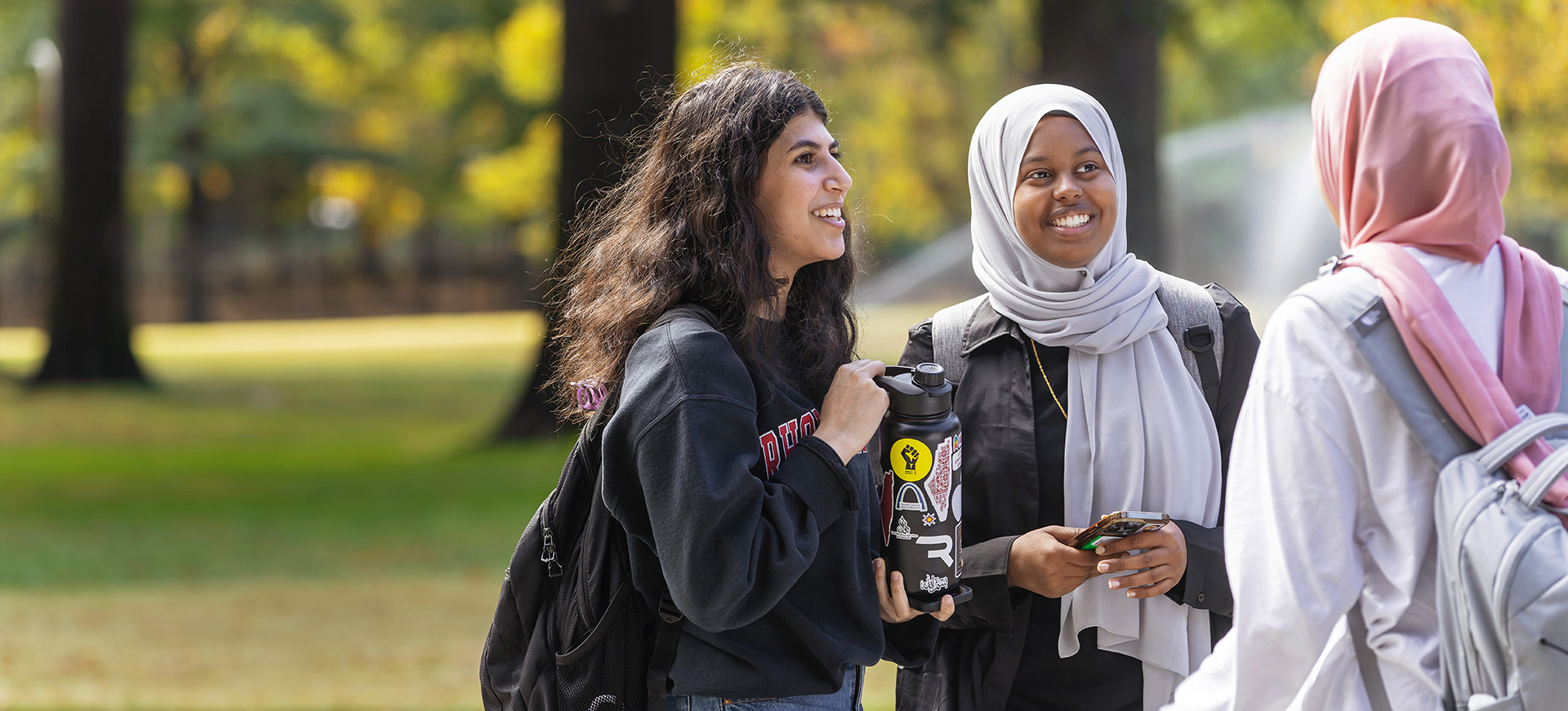 a smiling roup of three students, two in head scarves