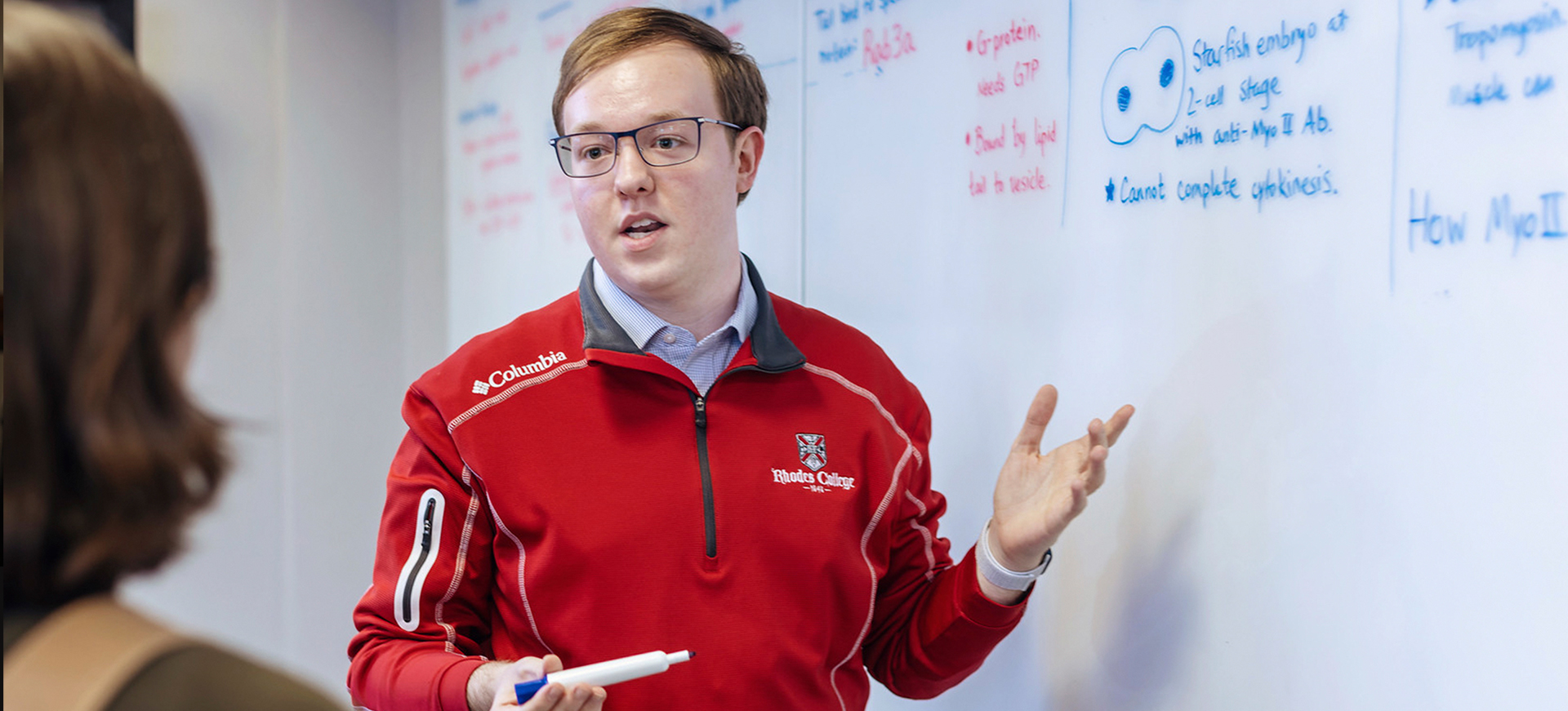 a young man gestures at a whiteboard