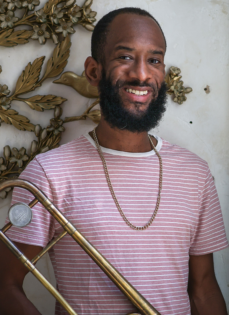 a smiling African American man with a beard holding a trombone