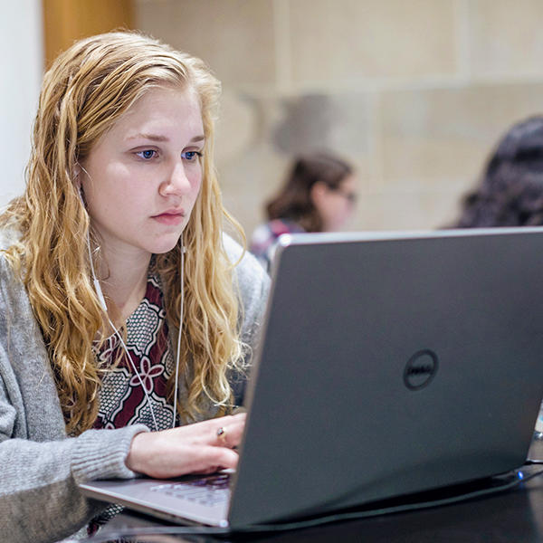 a female with long blonde hair listens to a computer through earbuds