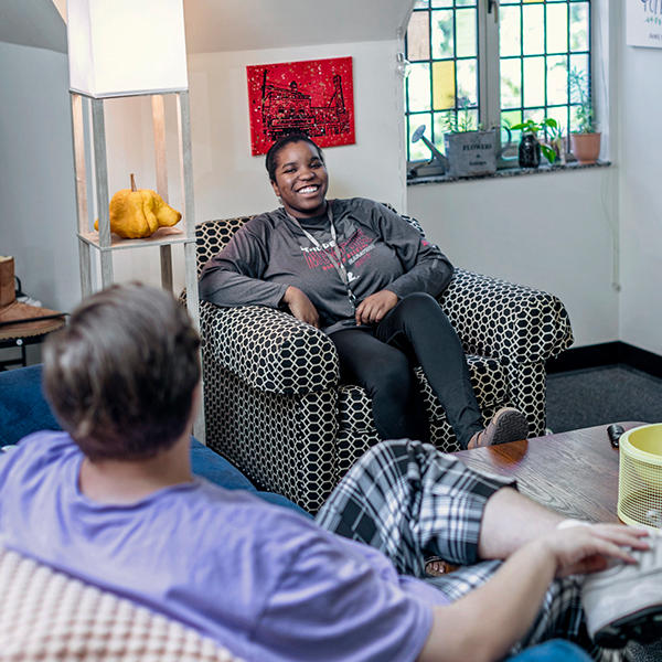 a male and female student chat in a living room