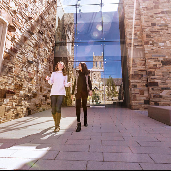 two female students walk in front of a stone and glass building