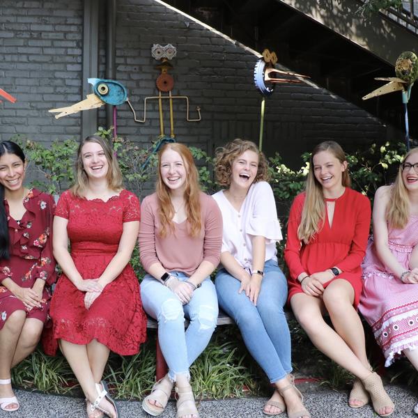 five young women sit on a bench and smile at the camera