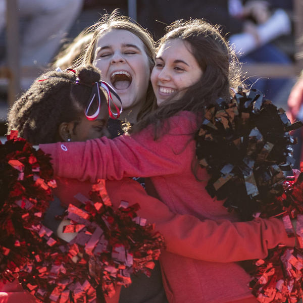 Cheerleaders hug at a football game.