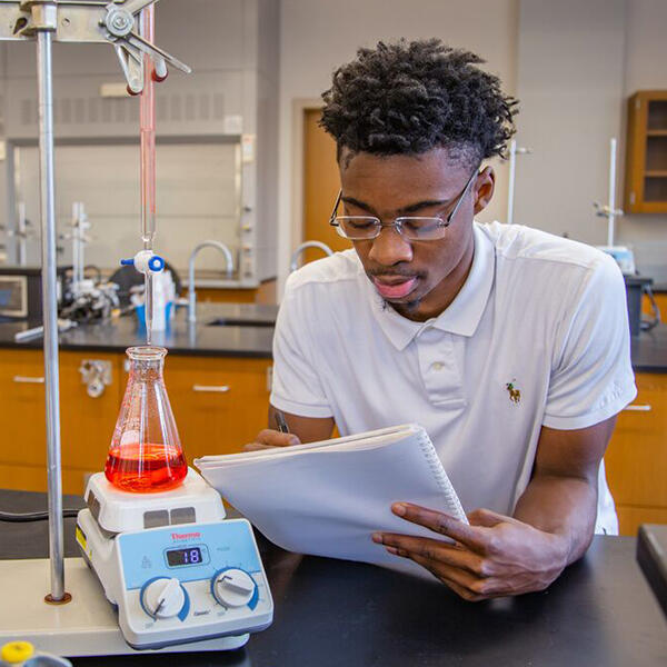 a young African American man takes notes on an experiment