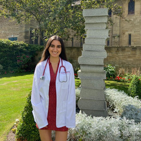 a young woman in a medical coat in front of a statue of stacked books