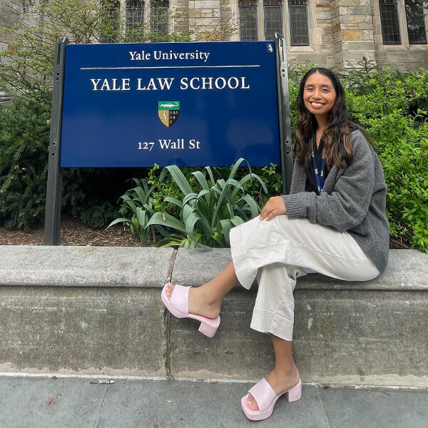 a yoiung woman with long dark hair in front of a sign that says Yal Law School