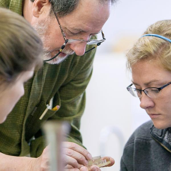 a male professor and two students look at a specimen