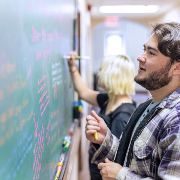 a student writes at a whiteboard