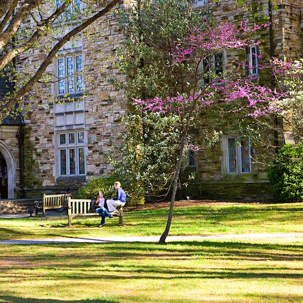 students talk on a bench outside of a Collegiate Gothic building