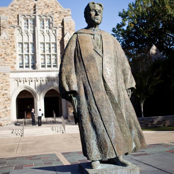 A bronze statue in front of a sandstone building with a slate roof.