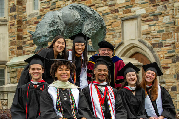 a group of graduates and a professor pose in front of a statue of a lynx