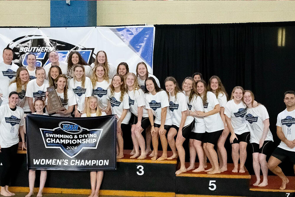 members of the women's swim team gather with a championship banner