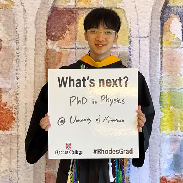 a student holds a sign that says grad school