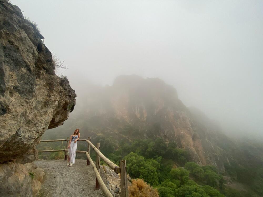 a young woman stands on a trail high in the mountains