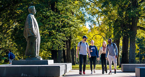 students walk in front of a statue of a man in academic robes