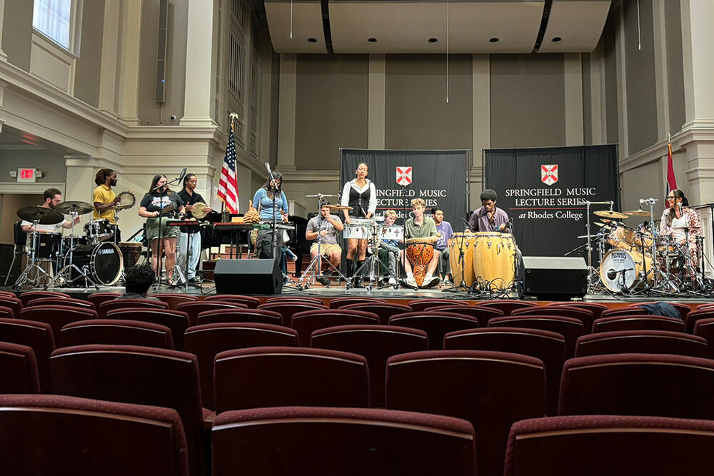 students and a guest play percussion instruments on a stage